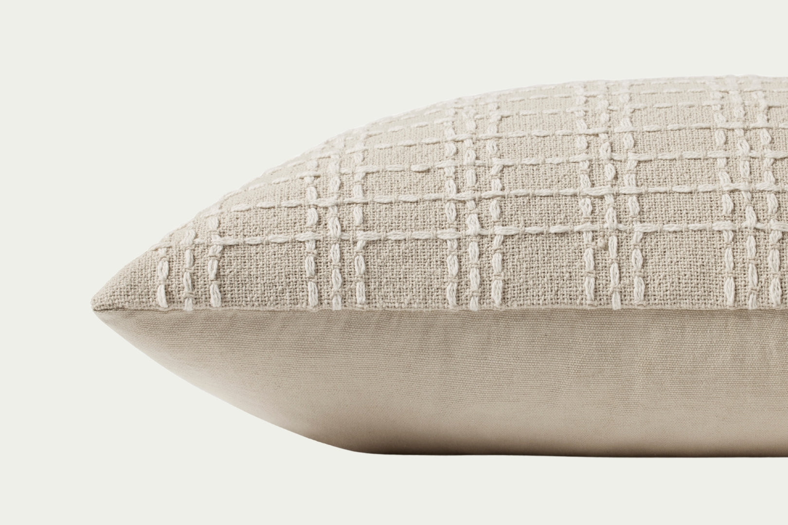 This beige and ivory lumbar throw pillow features a stitched grid design for texture. Made of cotton, it measures 16 by 26 inches, perfect for styling in living rooms and bedrooms.