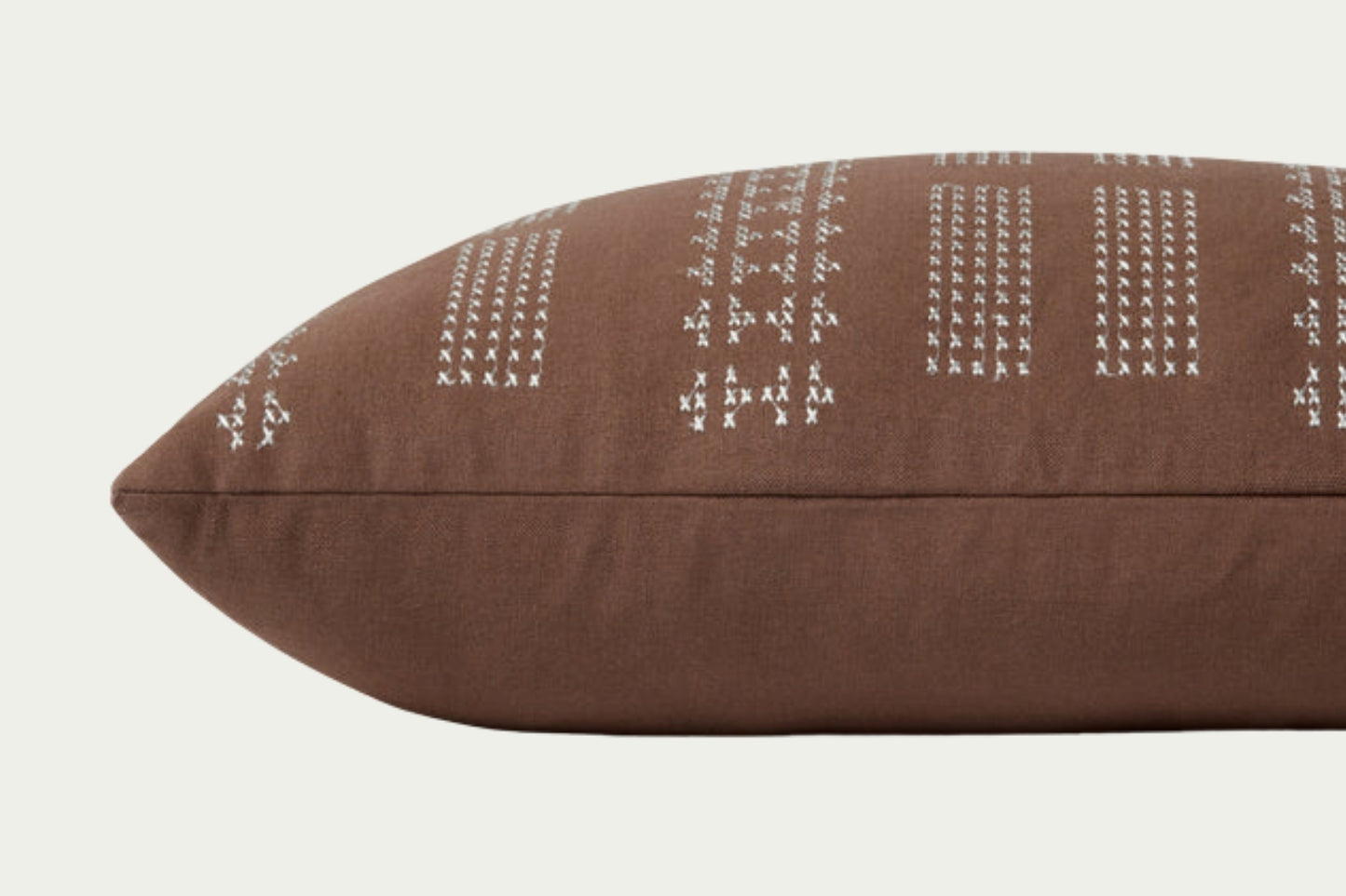 Geometric embroidery that draws the eye toward it. In Clay and Mist, a warm neutral brown with off-white details in a 35-inch by 13-inch rectangular throw pillow.